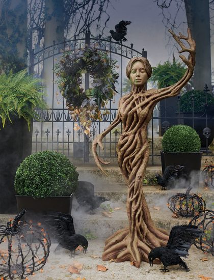 A woman made of branches poses in front of a mysterious and eerie scene.